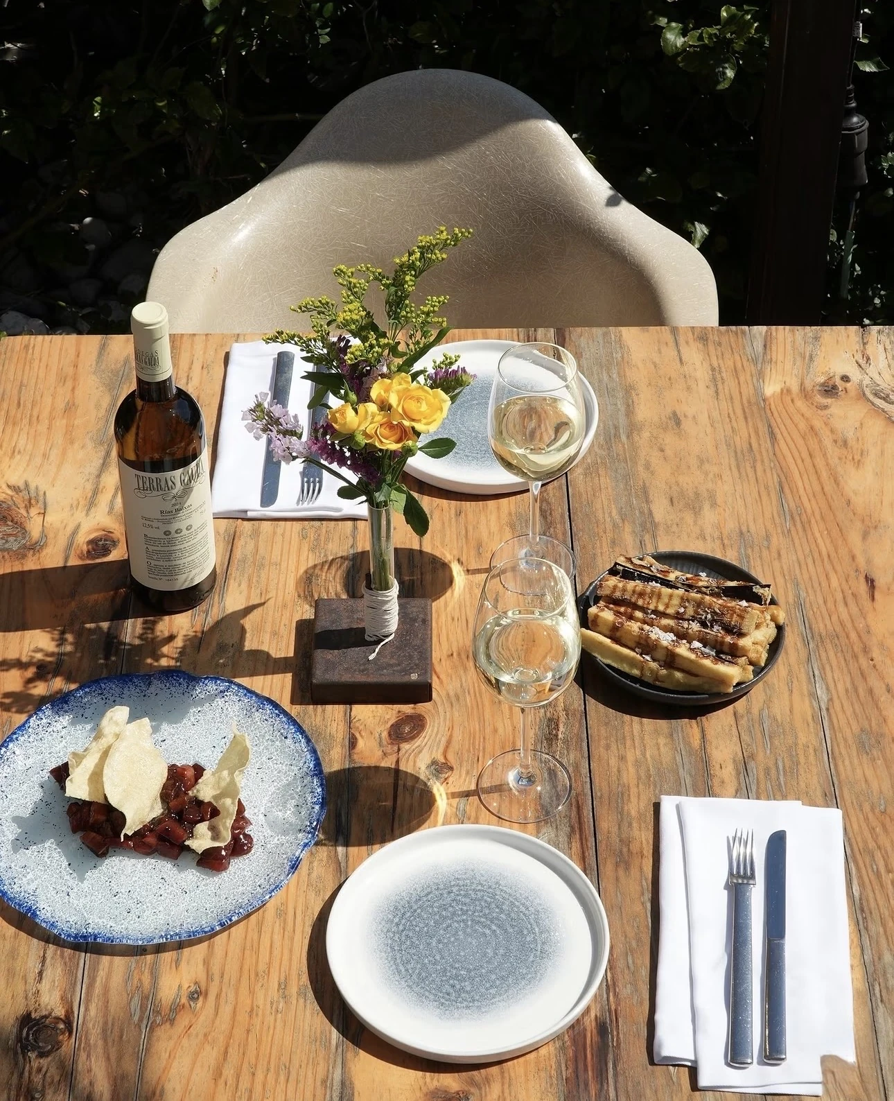 Mesa de madera al sol con albariño y flores