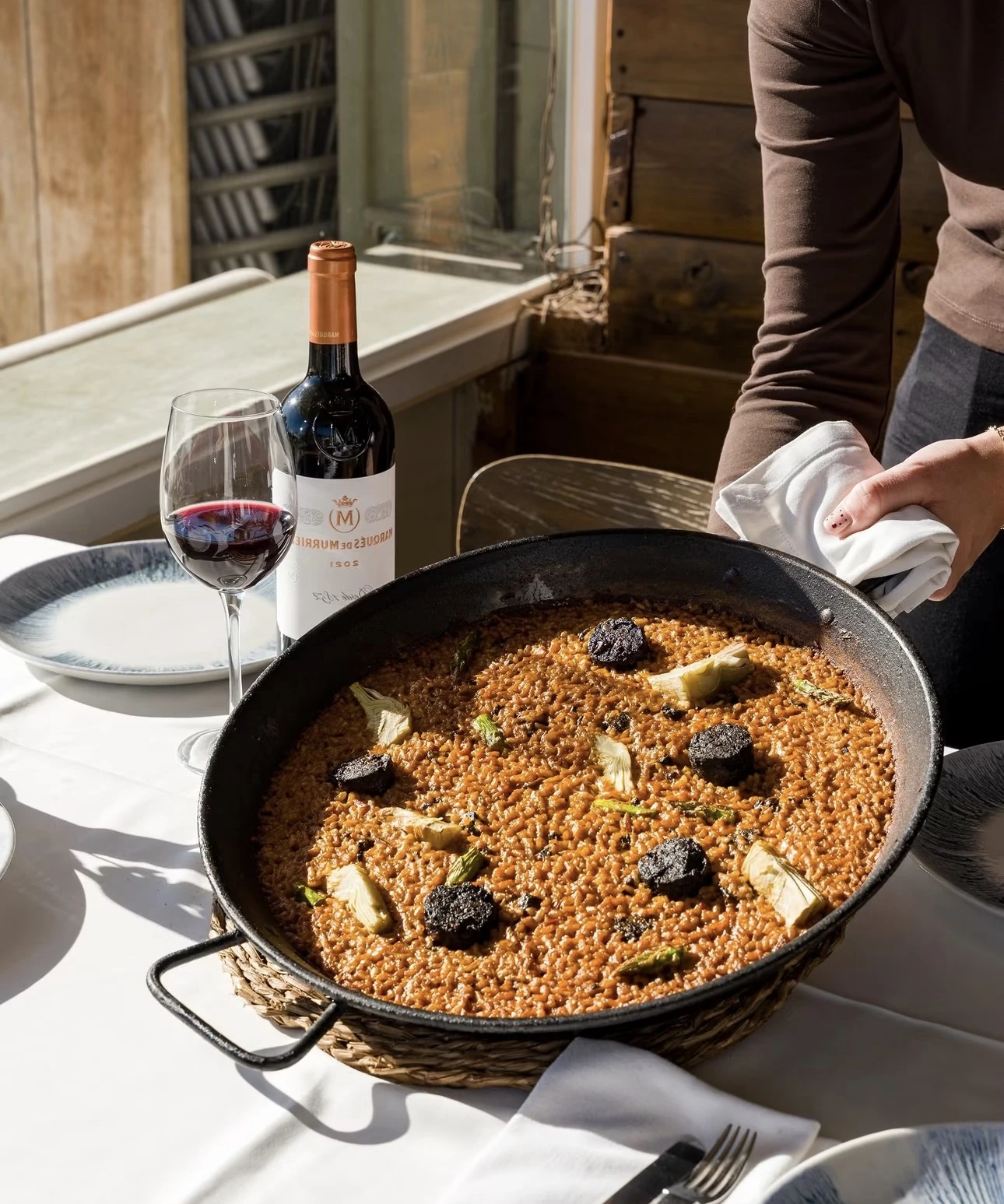 Arroz con botifarró, alcachofas y espárragos en paellera, con una copa de tinto